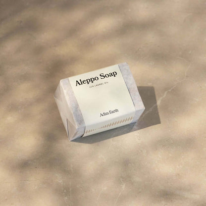 Aleppo soap bar on stone surface, showcasing natural skincare packaging under soft lighting.