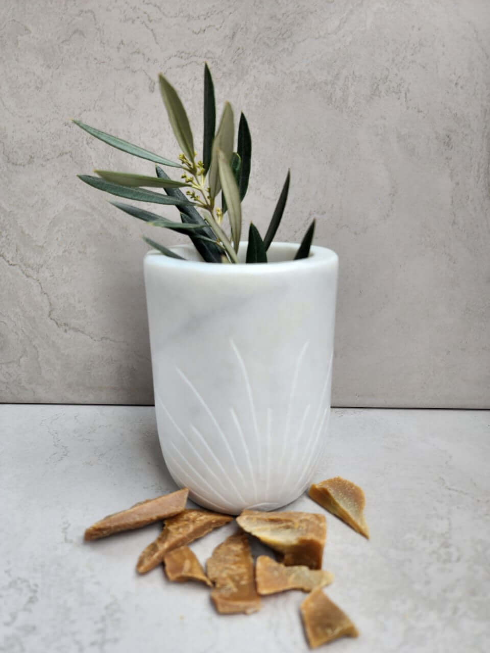 White marble vase with olive branches and soap fragments on a gray marble surface.