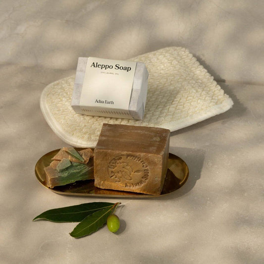 Aleppo soap bar and natural loofah duo displayed elegantly on a tray with olive leaves, enhancing a revitalizing bath experience.